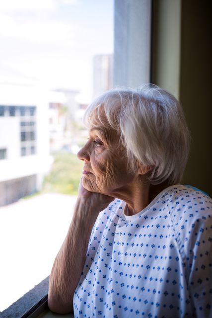 Thoughtful senior patient looking through window in hospital