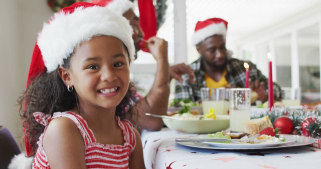 Portrait of smiling african american girl wearing santa hat celebrating holiday meal with family. family christmas time and festivity together at home.