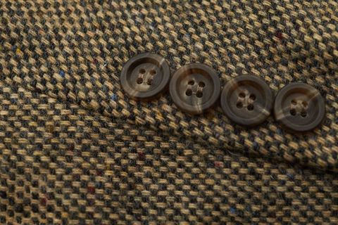 Rustic brown tweed jacket close-up showing four buttons and textured wool fabric detail