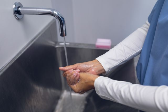 Mid section of female surgeon washing hands on sink at hospital