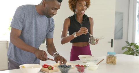 African american couple preparing healthy fruit yogurt bowls at modern kitchen island