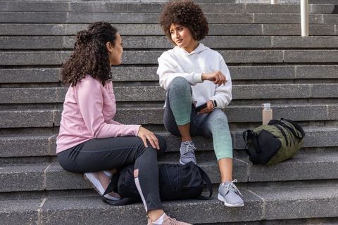 Friends chatting on urban steps during workout break wearing hoodies and athletic gear