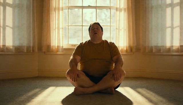 Sunlit man meditating in empty room with large multi-pane window