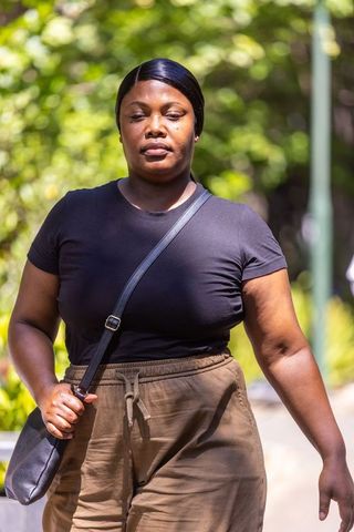 Woman walking confidently on sunlit park path wearing black t-shirt and crossbody purse