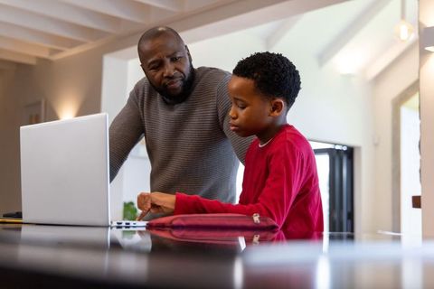 African american father helping son with homework on laptop at kitchen island
