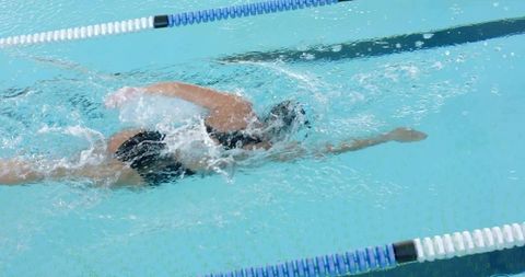 Mature woman swimming freestyle in turquoise pool lane, training and generating splash
