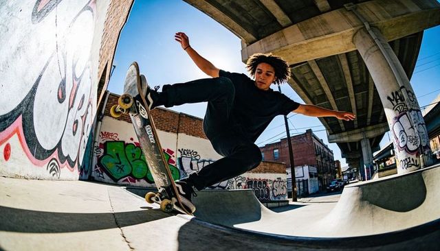 Skater launching over bowl under urban overpass performing midair skateboard trick