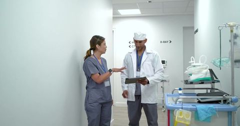 Healthcare team discussing patient care in hospital hallway reviewing digital tablet