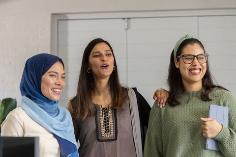 Multicultural women smiling, chatting and collaborating in contemporary office workspace