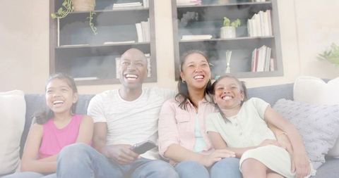 Laughing family sitting on couch enjoying movie night together in cozy living room