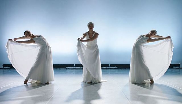 Three dancers performing lyrical ballet in flowing white gowns under dramatic backlight