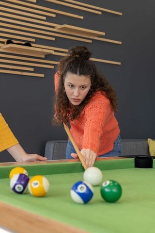 Young woman aiming pool cue while friends watching in modern game room lounge