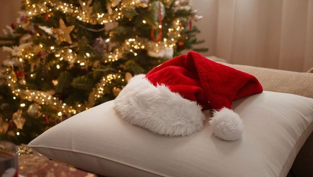 Santa Hat Resting on Cushion by Lit Christmas Tree Cozy Holiday Living Room Scene