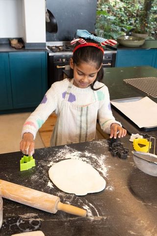 Indian girl baking cookies in home kitchen rolling dough and using cookie cutters