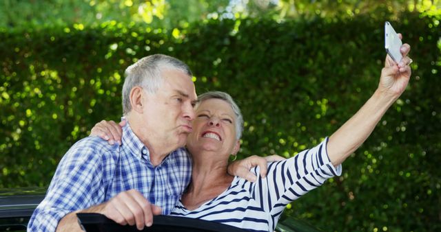 A senior Caucasian couple is taking a selfie together, with the man playfully puckering his lips and the woman smiling broadly, with copy space. Their joyful moment captures the essence of aging gracefully and cherishing memories.