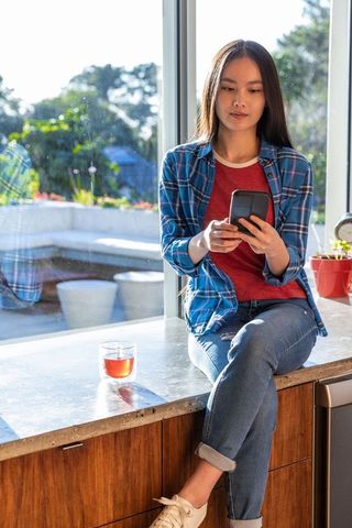 Young Woman Relaxing with Smartphone in Sunlit Kitchen Loft