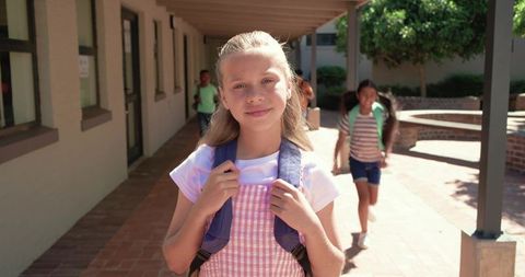 Sunlit school courtyard student standing with backpack smiling, elementary campus portrait
