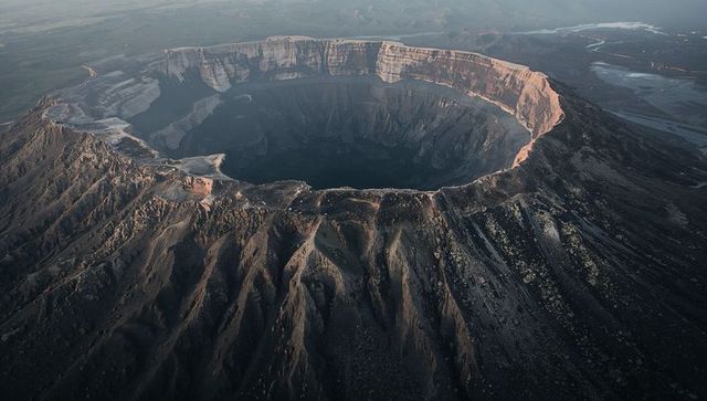 Aerial view showing massive volcanic caldera with terraced cliffs and shadowed basin