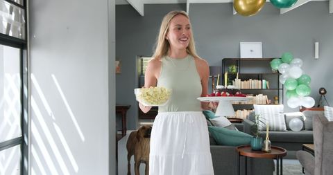 Woman joyfully carrying snacks and cake in festive room