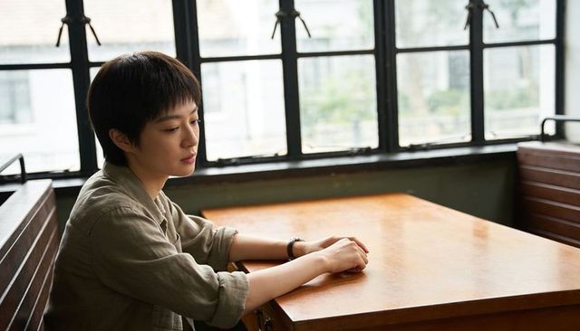 Contemplative asian woman sitting in cafe booth by window, olive shirt, wristwatch