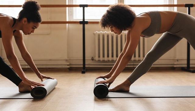 Partners rolling yoga mats and stretching before barre class in bright wellness studio