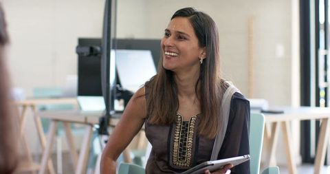 Indian professional wearing kurta and dupatta smiling in team meeting holding tablet