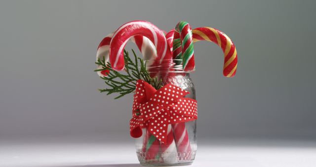 Candy canes in a jar decorated with a festive red ribbon and greenery, with copy space. Perfect for conveying the sweet and joyful spirit of the holiday season.