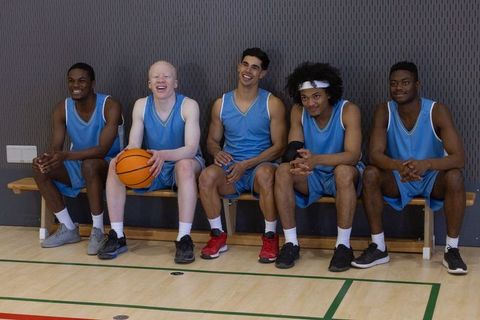Diverse basketball team relaxing on bench in gym