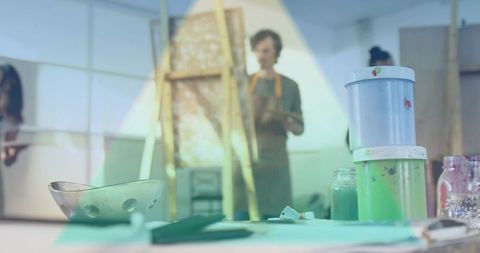 Stacked paint jars on studio table with blurred artists painting in background