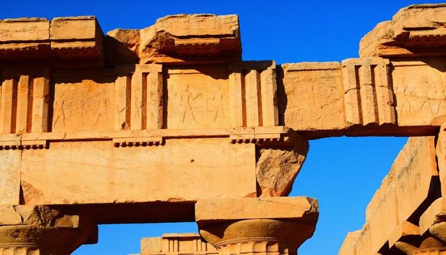 Ancient sandstone temple fragment showing carved relief panels and lintels under blue sky