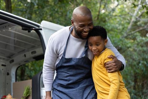 African american market vendor embracing son beside cargo van with fresh produce