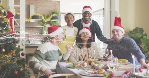 Multicultural friends celebrating Christmas dinner wearing Santa hats around festive table