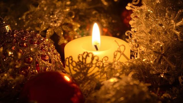 Glowing pillar candle casting warm light among gold filigree bauble and sparkling tinsel