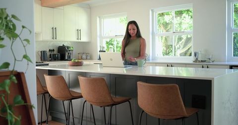 African american woman working remotely at bright minimalist kitchen island with laptop