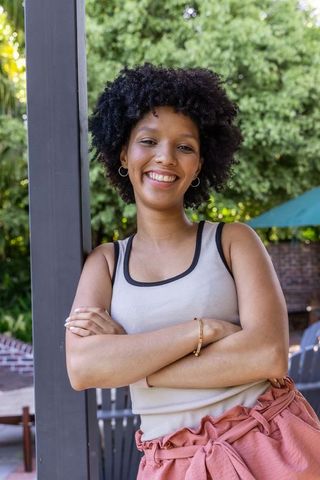 African american woman smiling and leaning with arms crossed on patio, casual summer lifestyle