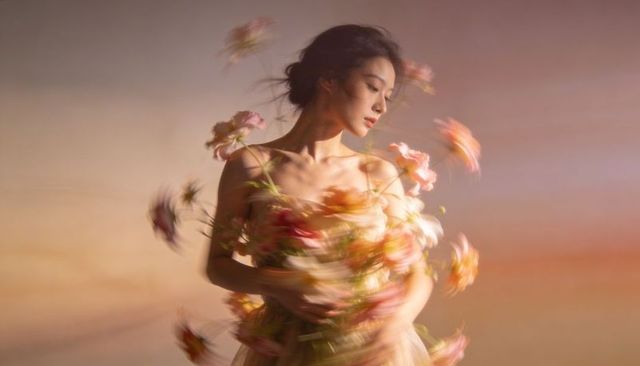 Spinning asian woman embracing swirling flowers in pastel tulle dress, ethereal motion