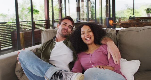 Happy diverse couple sitting on couch in living room, watching tv, embracing and smiling. spending free time together at home.