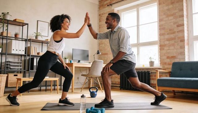 Young couple giving high-five while lunging during home workout in bright living room