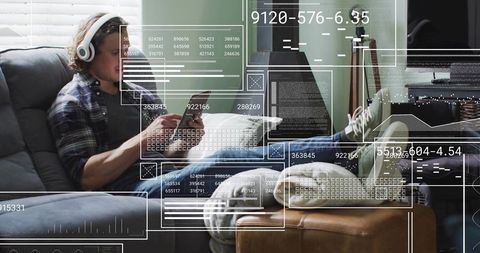 Young man reclining on sofa wearing headphones and using smartphone with hud overlay