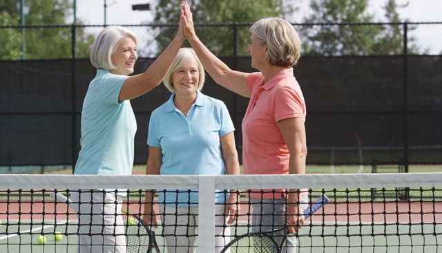 Senior women high-fiving at tennis net after doubles match