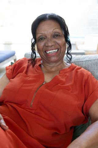 Smiling senior african american woman relaxing on sofa in rust-orange top, cozy portrait