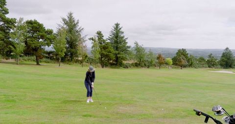 Woman lining up golf shot in scenic fairway with golf cart nearby