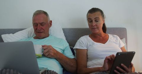 Senior Couple Using Technology Comfortably in Bed