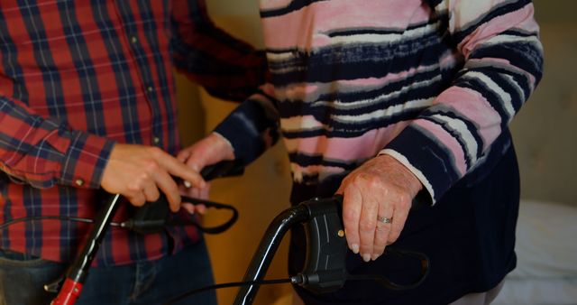Caregiver assisting elderly woman with walker indoors. Male hands provide support and guidance for elderly woman using mobility aid. Ideal for content related to senior care, healthcare services, elderly support, and aging.