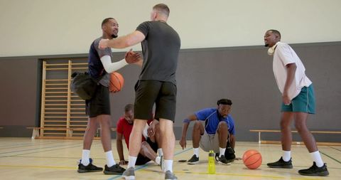 Diverse male friends talking and teaming up on indoor basketball court during training