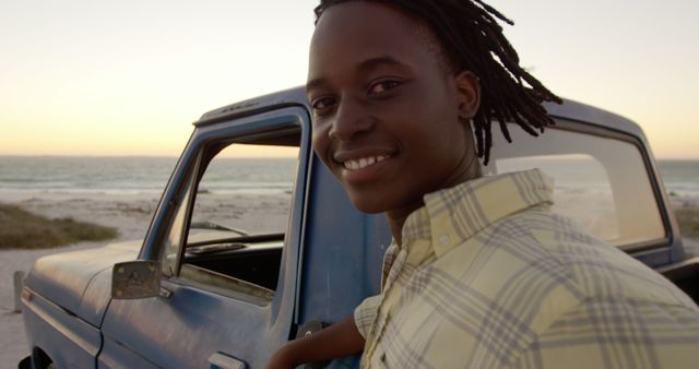 Smiling young man standing by vintage blue truck near beach at sunset - Download Free Stock Images Pikwizard.com