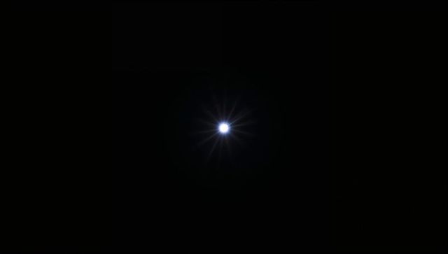Glowing starburst light radiating from center in dark sky with halo and lens flare