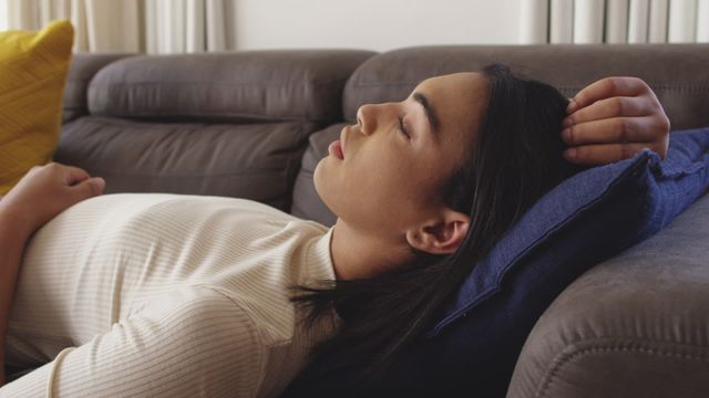 Person lying comfortably with eyes closed on a couch, exuding a sense of peace and relaxation. Ideal for use in content related to home living, relaxation techniques, solitude, or the importance of resting for mental well-being. Suitably reflects themes of comfort and personal time.