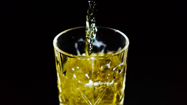Close-up of golden liquid being poured into a crystal glass against a dark background. Perfect for use in advertisements for beverages, bars, pubs, or alcohol brands, as well as in articles about drink preparation or luxury glassware.