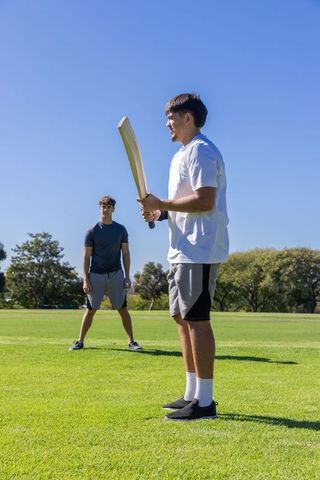 Two teammates practicing cricket on sunny park field, focusing on batting and teamwork